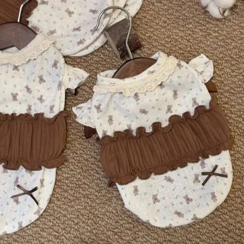 茶色のフリルの縁取りが施された白い犬用フローラルレースドレスで、小さなクマのプリントが特徴のパピー用シャツデザインです。