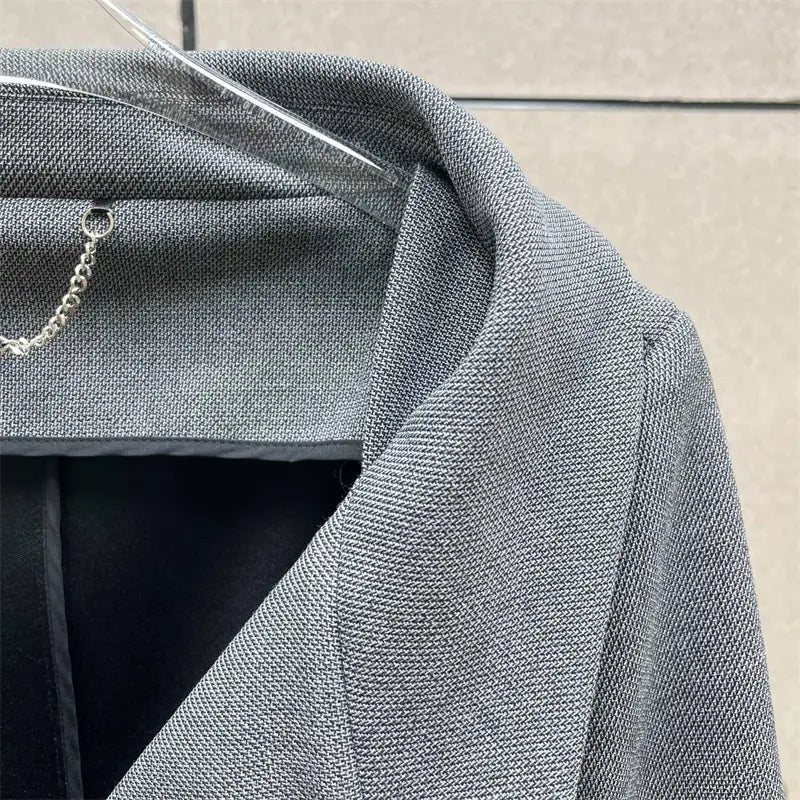 Jupe crayon grise taille haute de longueur genou au style Y2K associée à une veste blazer grise texturée présentant un motif tissé discret et un détail de chaîne argentée au niveau du col