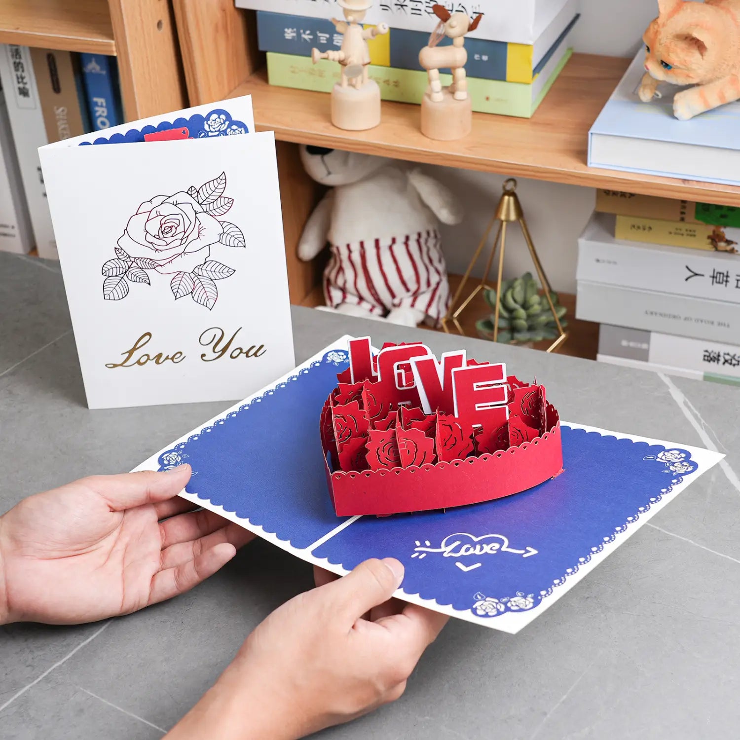 Carte de la Saint-Valentin 3D à effet pop-up en papier découpé rouge, richement travaillée, façonnée en forme de cœur, portant le mot « love » et des motifs de rose pour salutation en couple romantique.