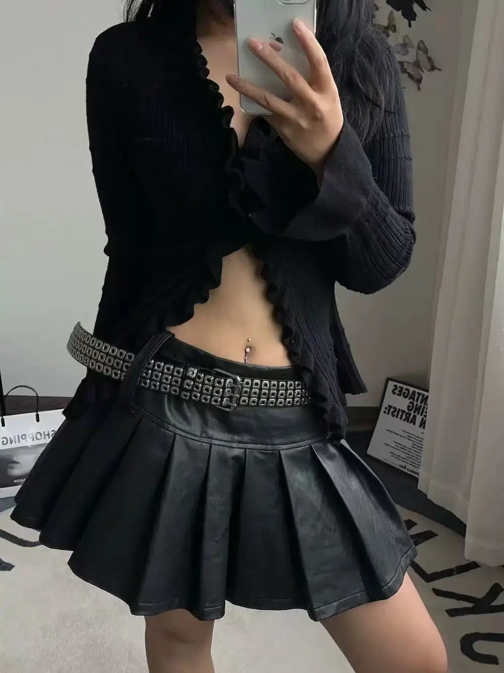 Black pleated leather mini skirt with a studded leather punk belt highlighting edgy fashion details.