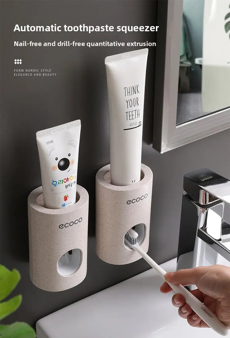 Beige textured wall mounted automatic toothpaste dispenser and holder set with two cylindrical ecoco branded holders holding a white tube of toothpaste.