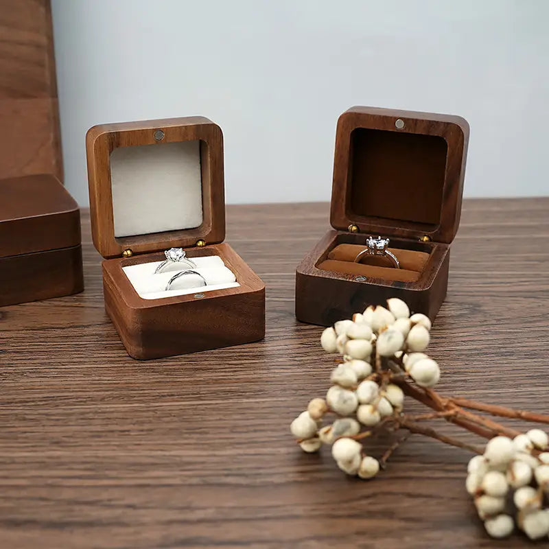 Boîte à bague en bois foncé pour proposition de mariage, présentoir pour bague d’engagement, avec couvercles à charnières affichant une bague d’engagement en diamant sur un velours blanc et une bague ornée à l’intérieur.