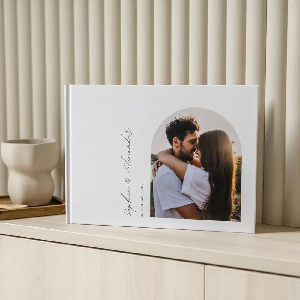 Elegantes Hardcover-Gästebuch für eine Hochzeit in Weiß als individuelles Fotoalbum, personalisiert, mit einem runden Foto eines Paares in inniger Umarmung und einer eleganten Handschrift auf dem Einband.