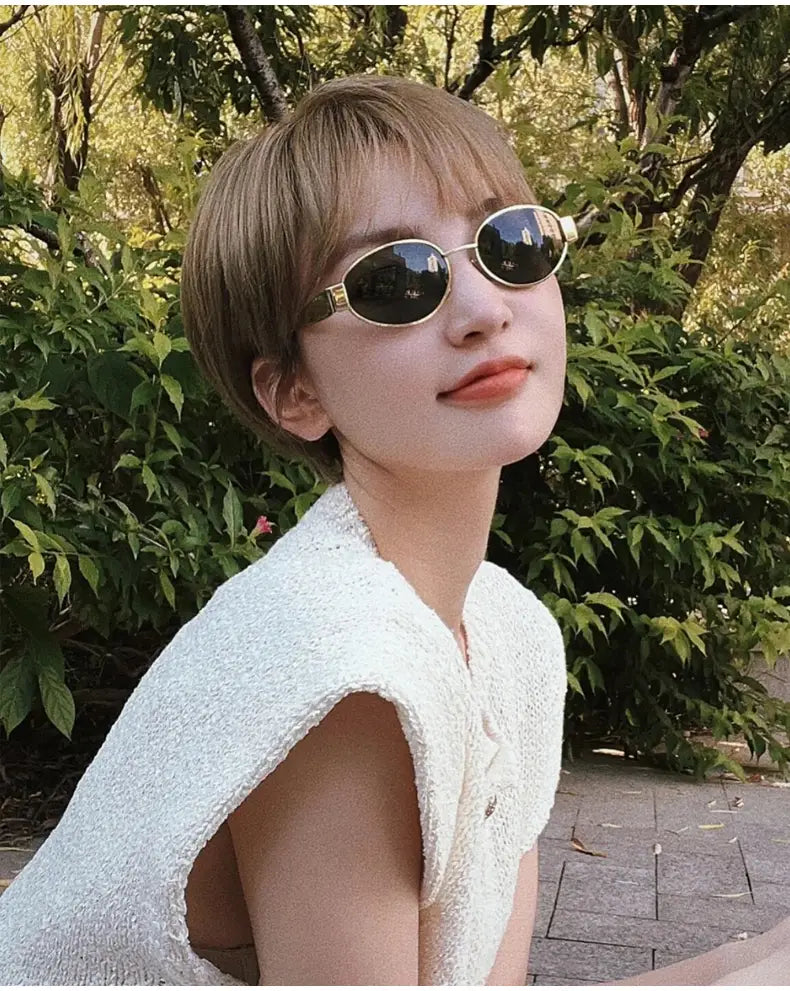 Gafas de sol ovaladas para mujer y hombre con monturas metálicas con acabado dorado y lentes oscuros.