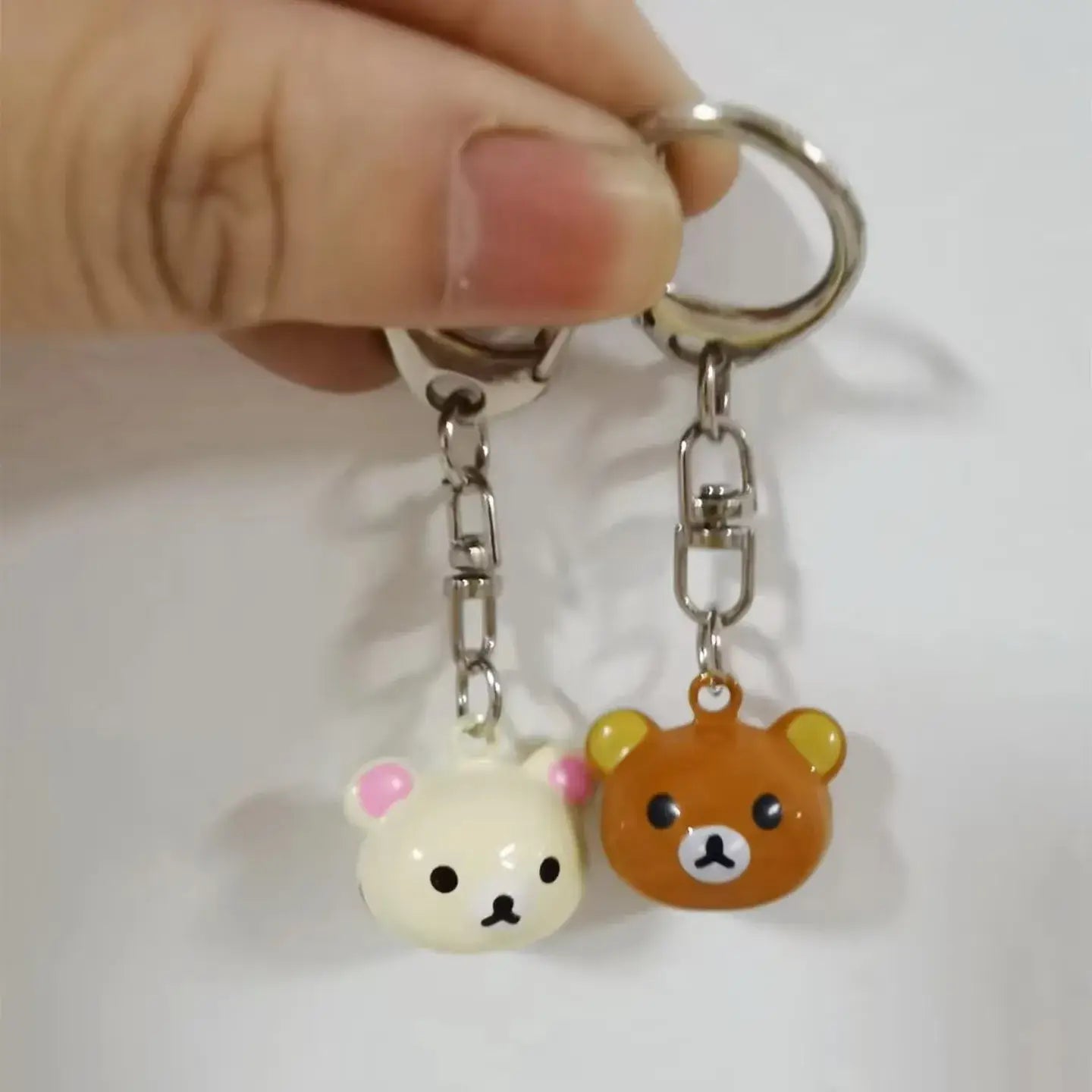 A pair of cute glossy plastic rilakkuma bear keychains featuring one white with pink ears and one orange character attached to silver metal rings.