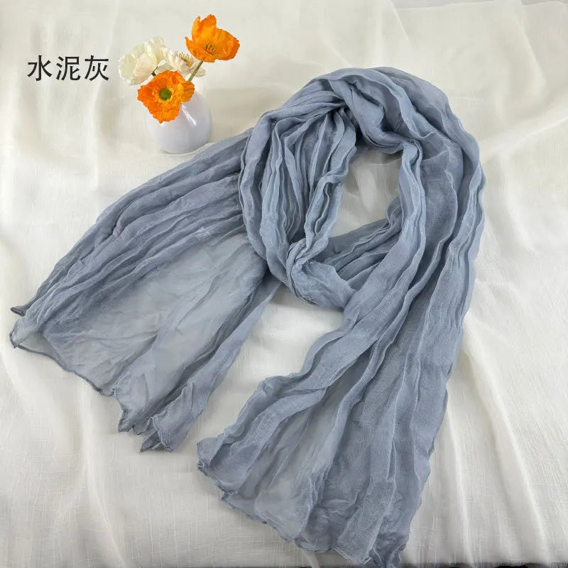 Écharpe en coton et lin plissé gris clair, douce et légère, avec un tissu légèrement texturé froissé et des bords délicatement effilochés.
