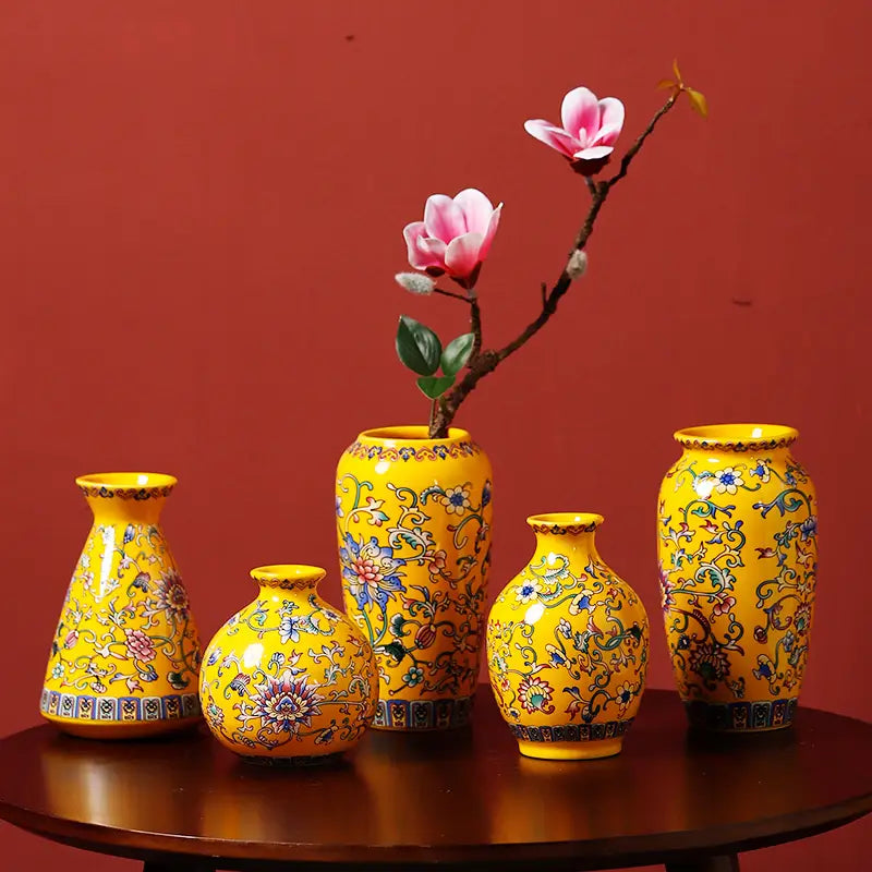 Un ensemble de cinq petites vases en émail de céramique, de couleur jaune éclatante, présentant des motifs floraux et de feuillages bleus-verts et violets complexes, reflétant un design de porcelaine chinoise d’inspiration ancienne.