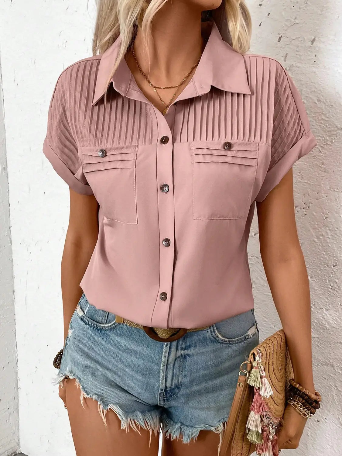 A soft pink short sleeve button up blouse for women featuring a pleated front and two chest pockets with short sleeve length.