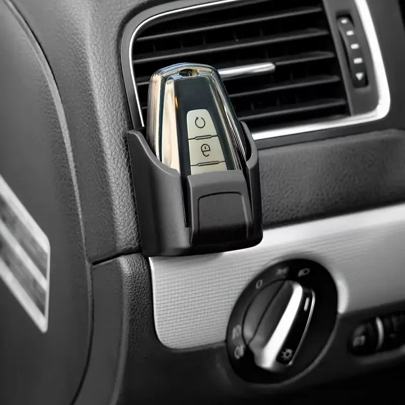Black plastic car key organizer dashboard storage box securely cradling a silver and black car key fob with two buttons.