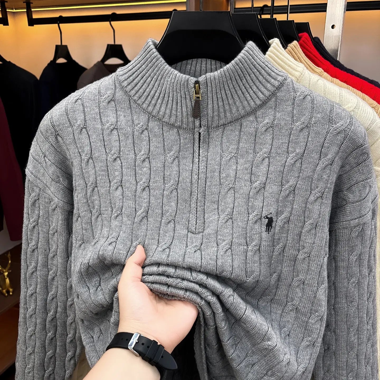 Herren-Designer-Sweater aus grauem Zopfmusterstrick mit halbem Reißverschluss, mit kleinem schwarzem besticktem Polo-Spieler-Logo auf der Brust.