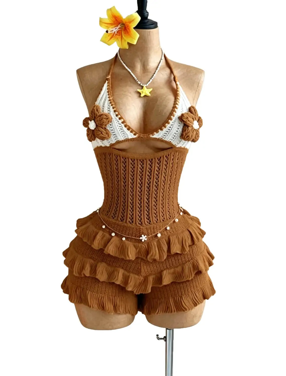 Brown knitted two-piece swimsuit featuring a white crochet halter top and ruffled shorts with crocheted flower details on the shoulders in a knitted ruffle halter romper summer playsuit.