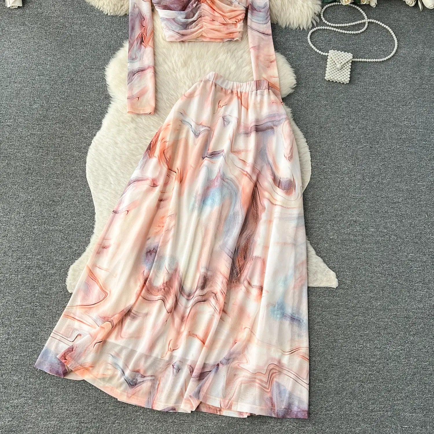 A flowing long-sleeved two-piece mesh skirt set with a marble print in soft pinks purples and blues on lightweight fabric featuring an elastic closure.