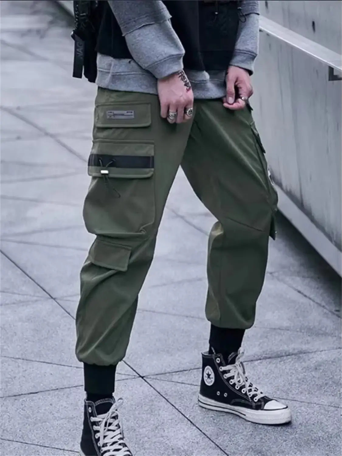 Pantalones tipo jogger cargo verde oliva para hombres con múltiples bolsillos y detalles en correas negras, diseñados para estilo urbano y uso casual.