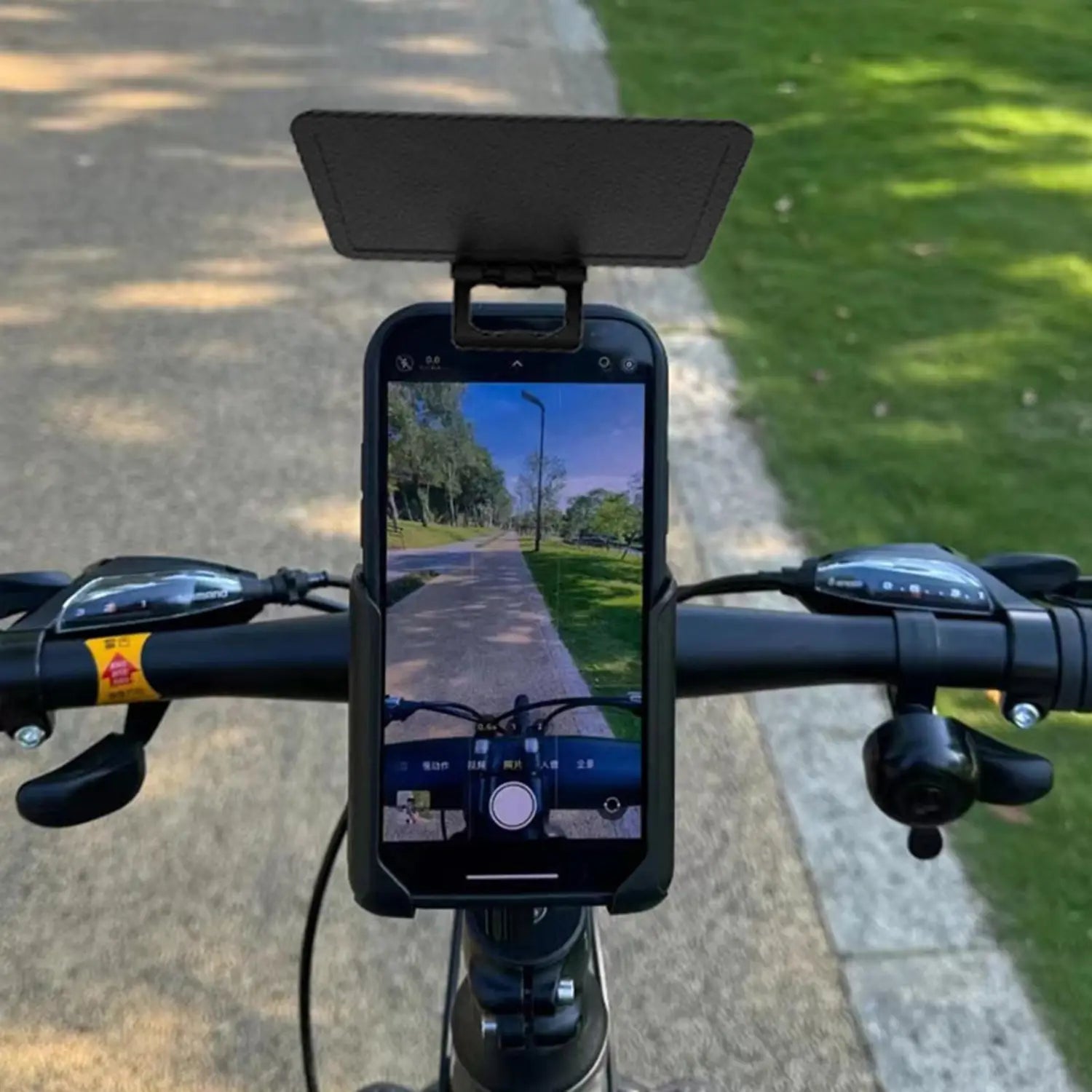 teléfono inteligente negro montado en un manillar de bicicleta con un protector solar para teléfono negro adherido que proporciona una cubierta de protección contra el deslumbramiento y la radiación UV