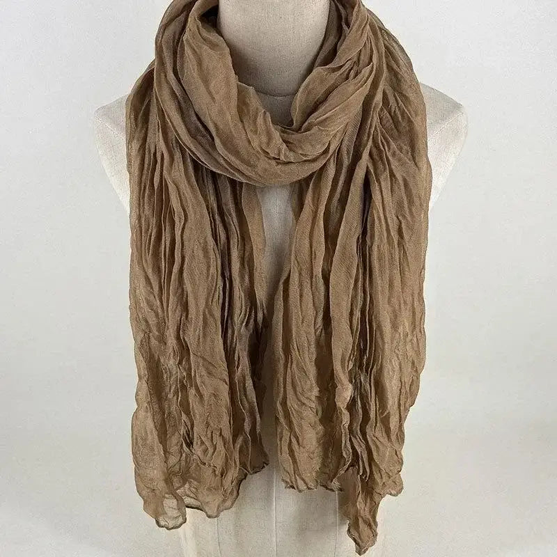 Una bufanda de algodón lino color beige suave con textura arrugada, drapeada alrededor del cuello de un maniquí, mostrando un chal de color sólido y transpirable para mujer.
