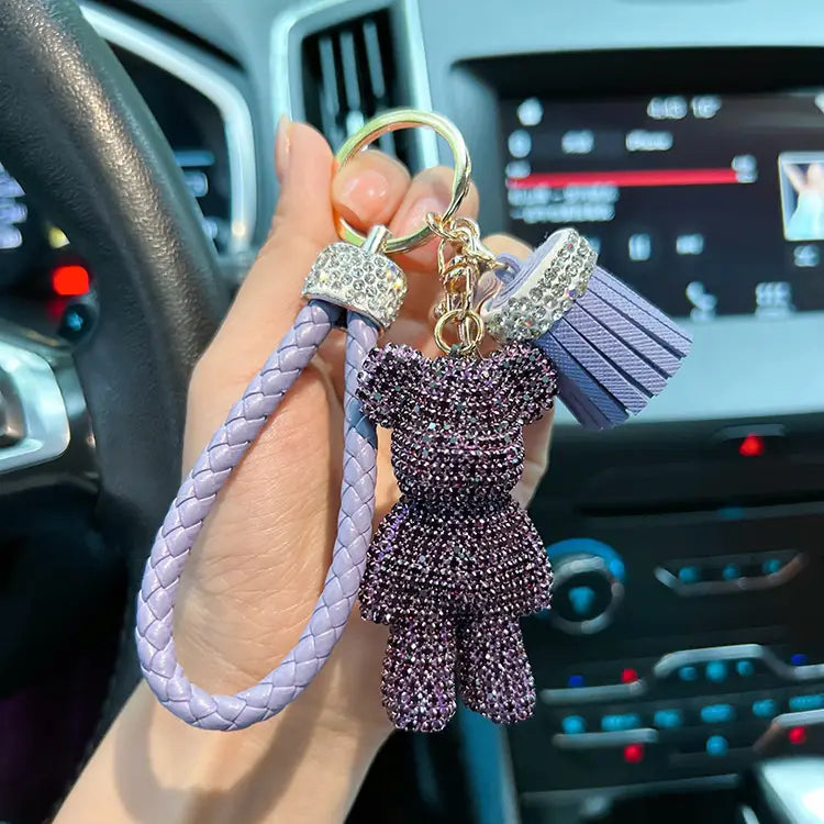 A lavender braided leather keychain with a sparkling purple rhinestone bear charm, matching tassel, and crystal-encrusted accents.