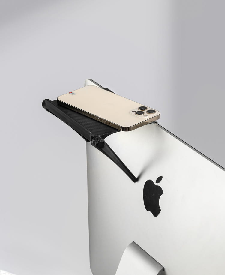 Black adjustable screen top storage shelf monitor stand made of durable material holding a gold-colored iPhone securely.