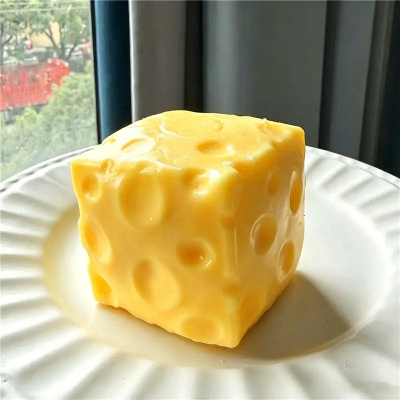 Un jouet sensoriel de type balle anti-stress en forme d’arachide, jaune vif, de forme cubique, évoquant le fromage, avec des perforations caractéristiques et une surface lisse et brillante