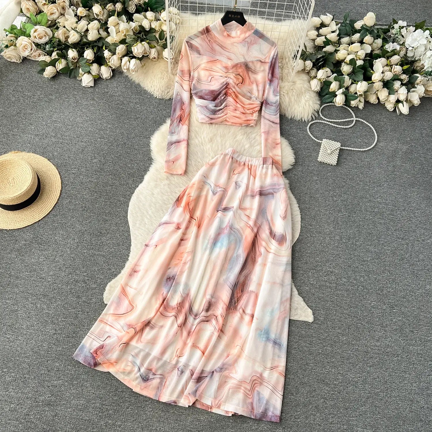 a flowing two-piece mesh skirt set with an abstract marble print in soft pink, peach, lavender, and gray hues featuring a high-neck long-sleeved top and elastic closure