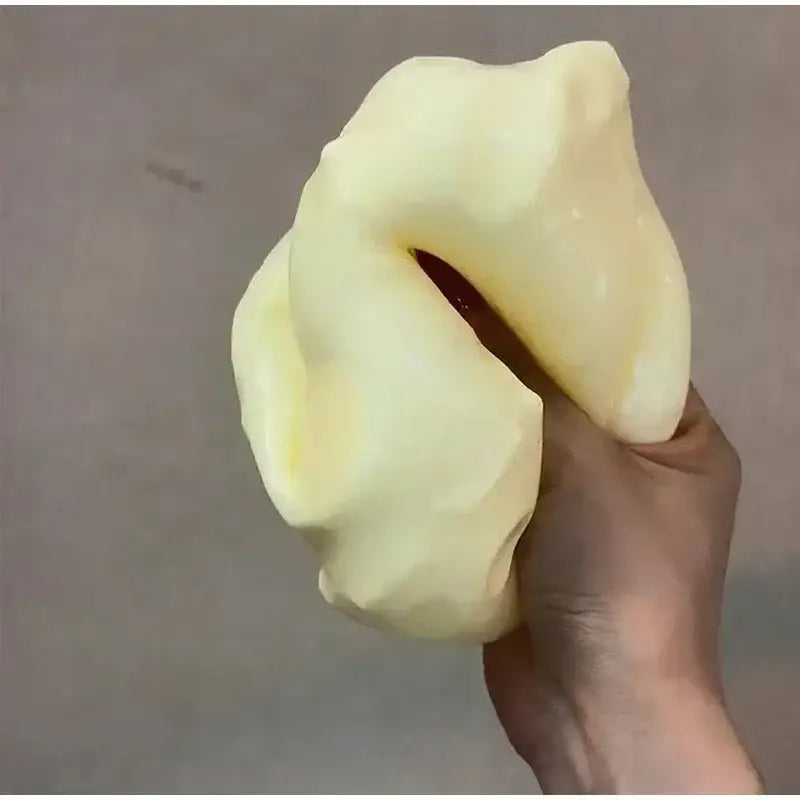 Una pelota antiestrés blanda, amarillamente pálida y elástica, con una superficie lisa ligeramente brillante, diseñada como un juguete antiestrés esponjoso con forma de queso amarillo.