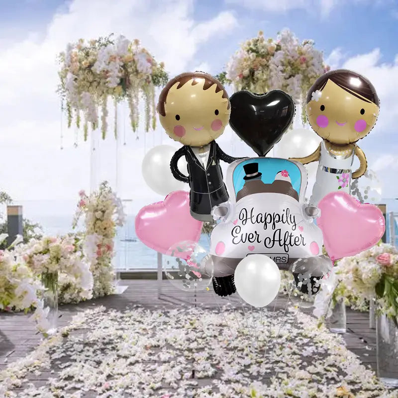 A whimsical wedding-themed balloon bouquet featuring cartoon groom and bride balloons, a black heart balloon, pink hearts, white balloons, and a central happily ever after scooter design for couple decor.