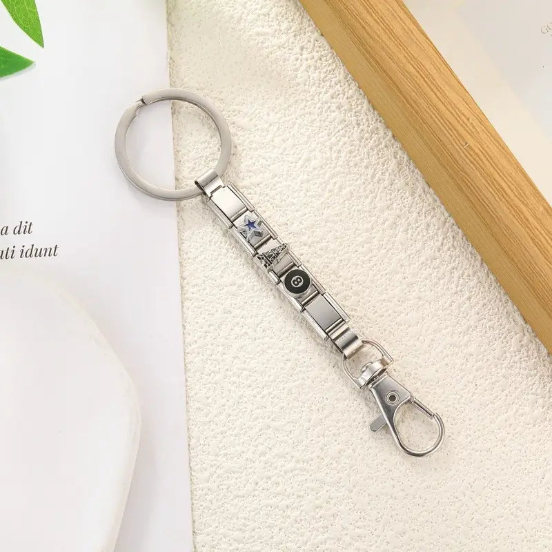 Llavero con dije de eslabones italianos de metal con acabado plateado, con un emblema en forma de estrella y circular, con una estructura de cadena modular elegante, diseñada para uso personalizado en bricolaje