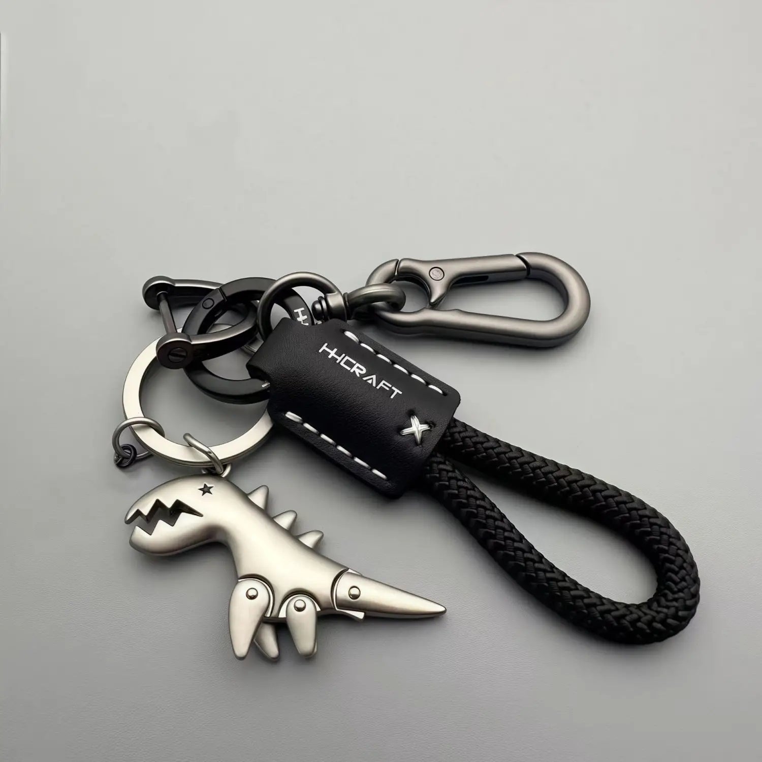 Silver dinosaur leather keychain bag pendant with a black braided leather strap and a black leather tag featuring white stitching.
