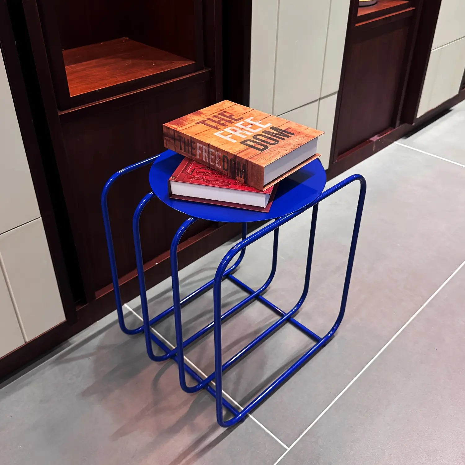 Blue metal side table with curved legs and circular top designed as a minimalist storage magazine rack.