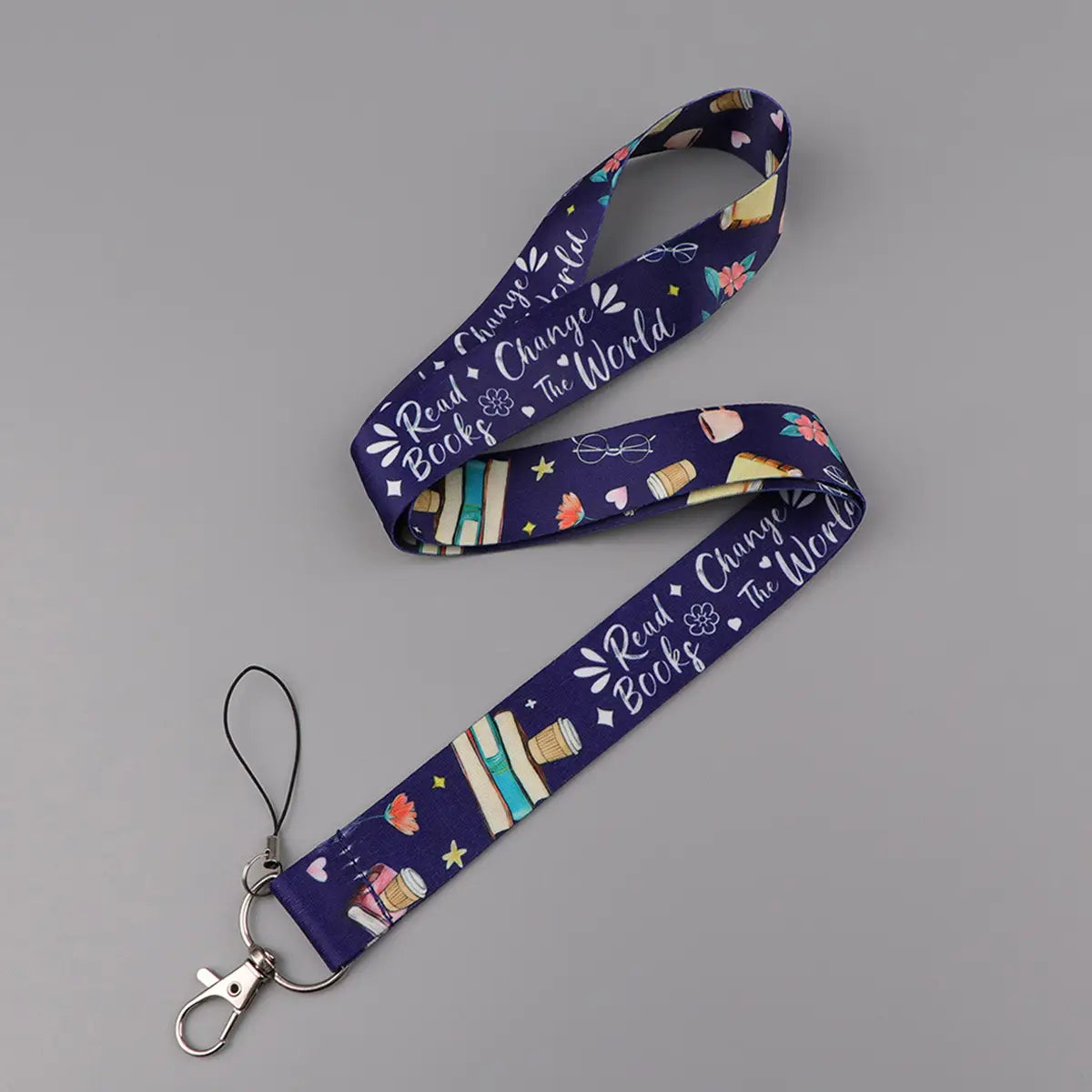 A navy blue book lover lanyard and ID card holder set featuring a repeating pattern of books coffee cups and the phrase read books change the world in white script.