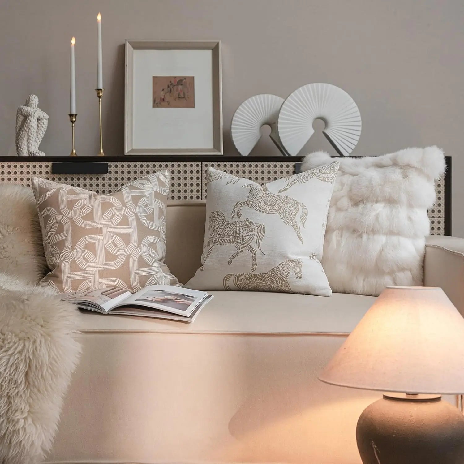 canapé beige avec housse de coussin de luxe couleur lin sec en jacquard géométrique, coussin rectangulaire, rehaussée de coussins d’appoint à motifs et à effet fausse fourrure, avec une lampe de table à lumière douce et un magazine ouvert sur le coussin.