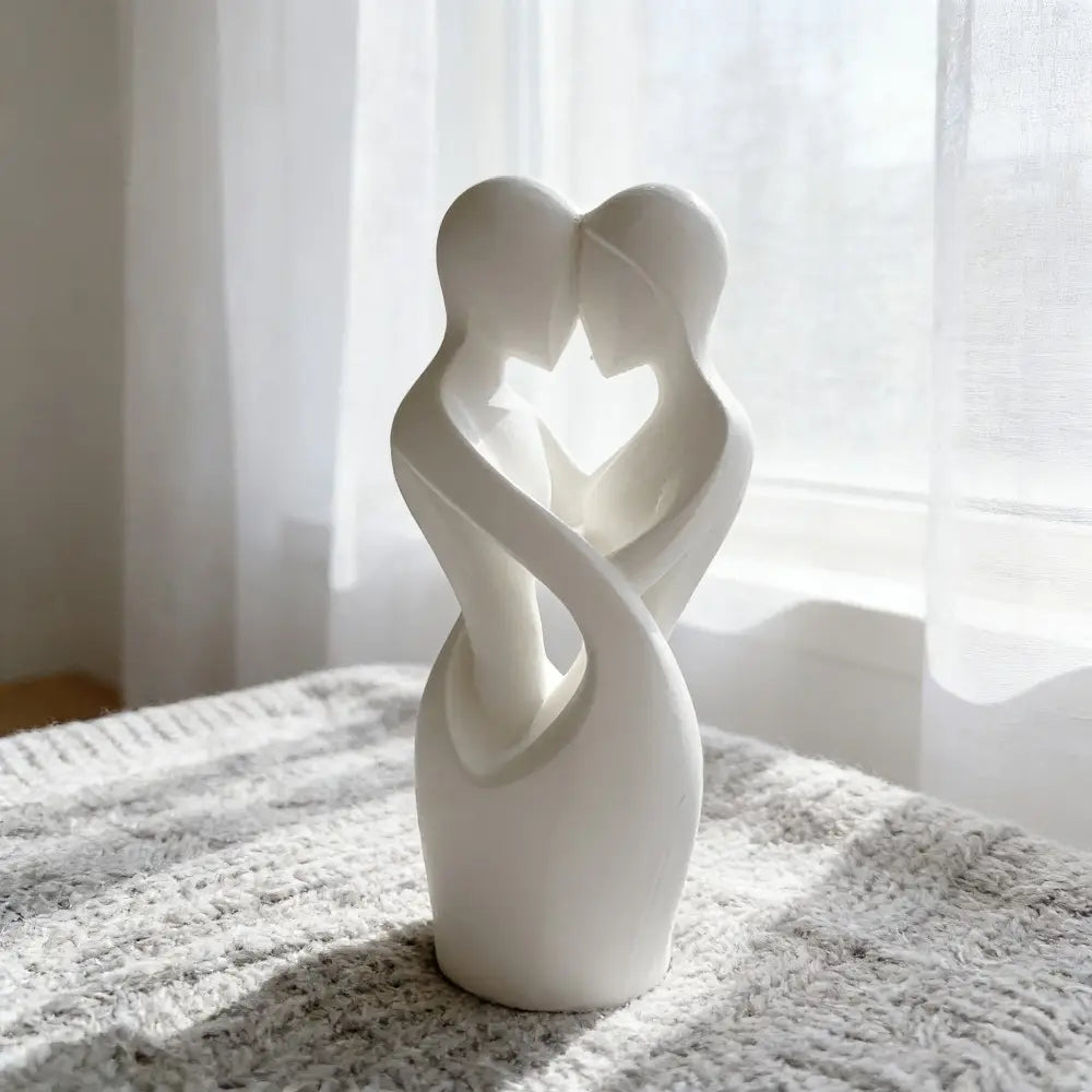 A smooth white ceramic sculpture of two abstractly intertwined figures forming a heart-shaped opening for modern decor titled Intertwined lovers heart sculpture.