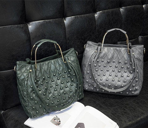 Bolso de hombro de cuero verde oscuro con diseño acolchado, tachuelas metálicas de tono dorado, asas de tono dorado y detalles de compartimento interior visible.