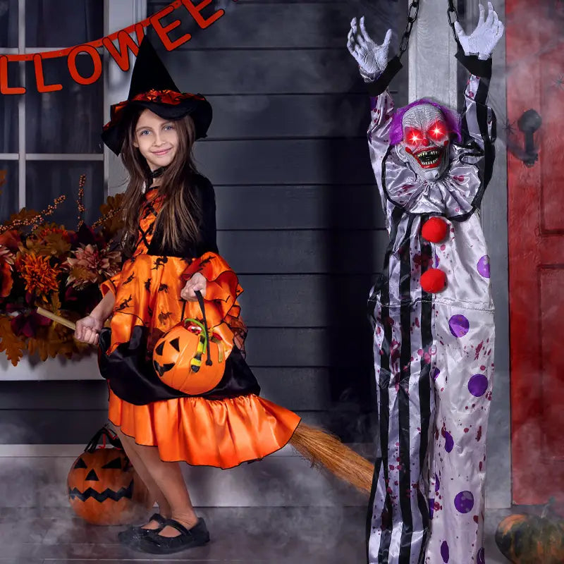 Kostüm einer Hexe in Orange und Schwarz mit einer Kürbis-förmigen Tasche; dargestellt mit einem hängenden Geist mit Sprachsteuerung, animiertem Clown für Halloween