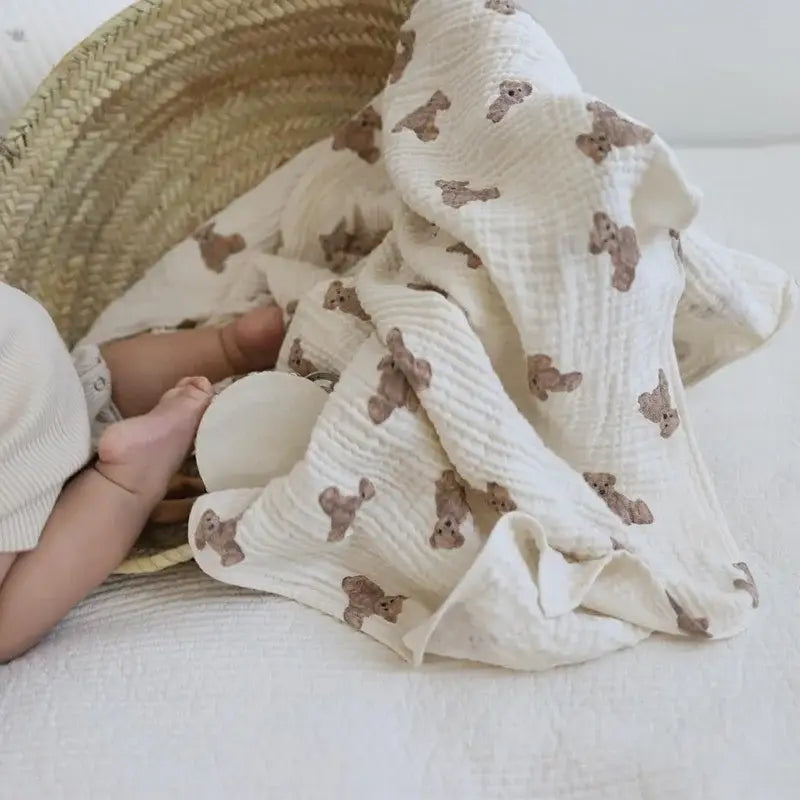 ein weiches Baby-Badehandtuch und eine Wickeldecke aus Muslin in sanftem Off-White mit Bärenmotiv; mit einer subtil strukturierten Webart und verstreuten braunen Teddybären
