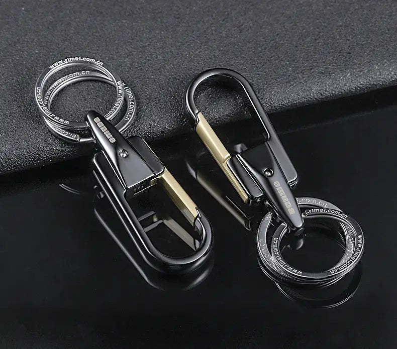 ステンレス製のキーホルダーリングとカラビナ風クリップを備えた、ブラックおよびゴールドの回転式カーキーチェーン。