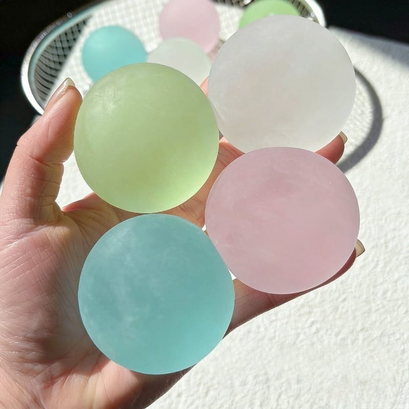 A hand holds several pastel-colored translucent blue mochi squeeze sensory fidget toy stress balls with a smooth matte finish.
