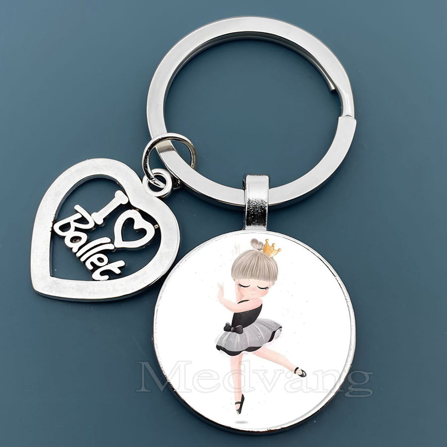 「I love ballet」と刻印された銀色のハート形チャームを備えたシルバーのバレエキーチェーン。グレーのチュチュを着たバレリーナのイラストが入った丸いガラスペンダント。