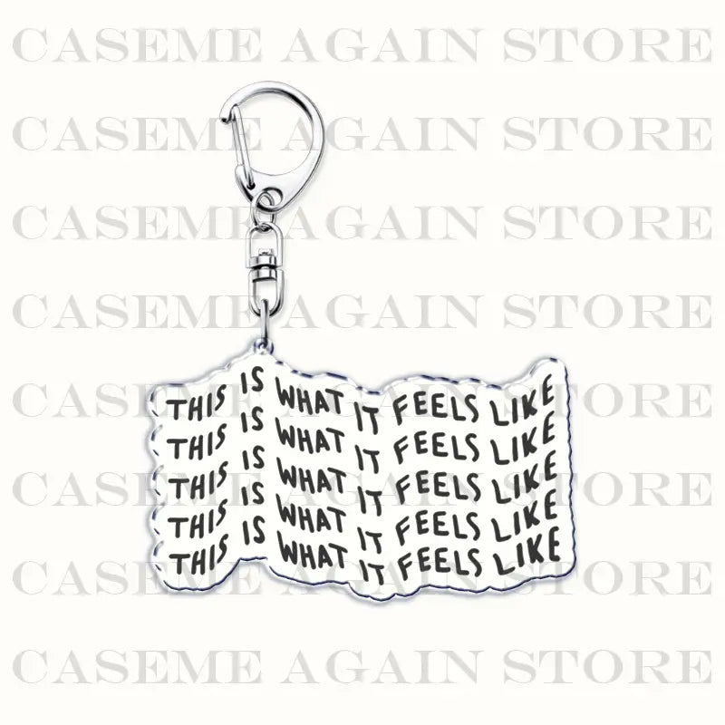 Silver metallic acrylic keychain shaped like a folded paper with the phrase this is what it feels like printed in black for Gracie Abrams anime fan gift.