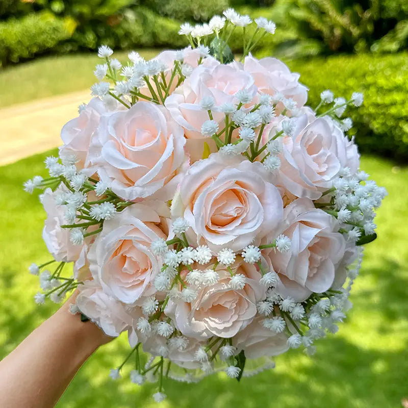 A delicate white silk rose wedding bouquet featuring soft peach-colored artificial roses accented with tiny white filler flowers lace and pearls.