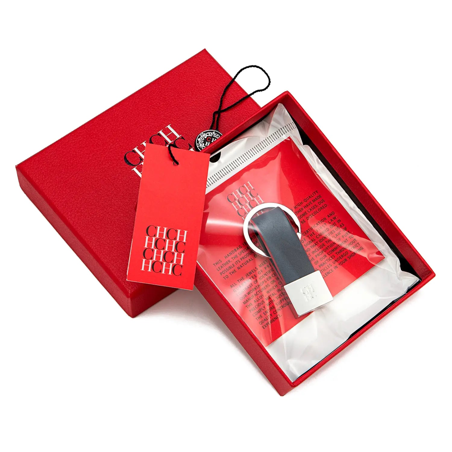 Elegante porta llaves de cuero negro con anillo metálico de tono plateado y una placa rectangular, presentado en una caja roja de marca, ideal como accesorio de equipaje minimalista.
