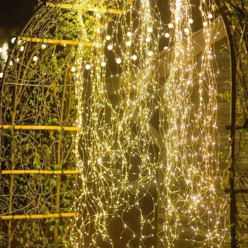 guirlandes dorées à ampoules à lueur chaude, descendant d'une treille arquée, avec du fil de cuivre, dans une configuration de guirlandes lumineuses solaires à DEL en fil de cuivre pour extérieur
