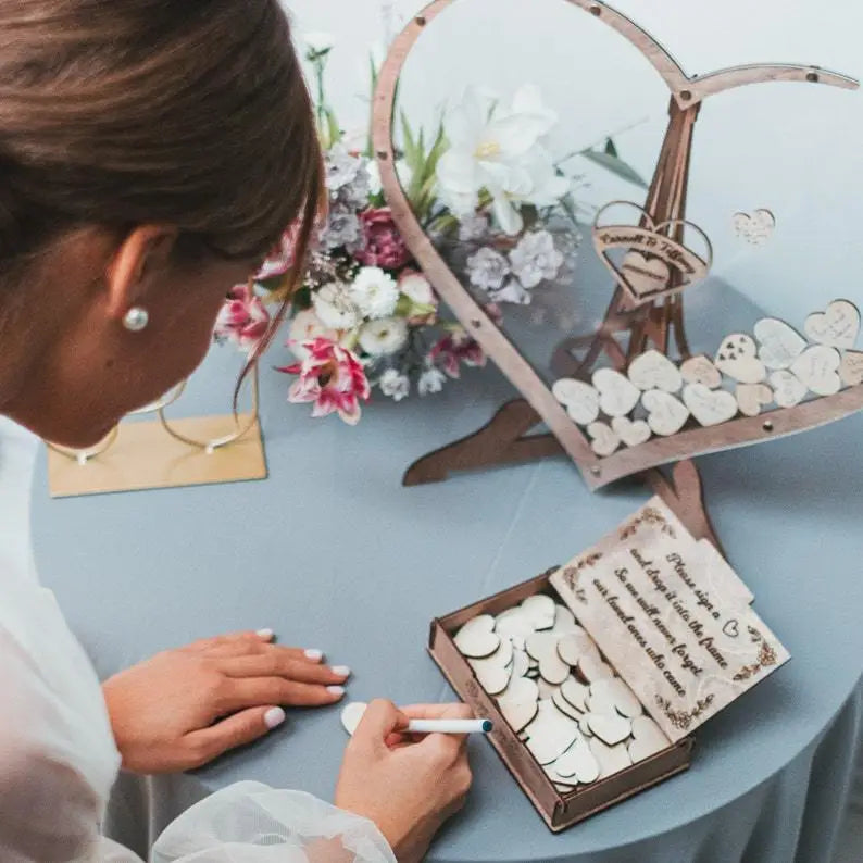 Boîte de dépôt pour livre d’or de mariage en forme de cœur en bois, avec des initiales gravées et des accents floraux décoratifs dans une teinte de bois naturel.