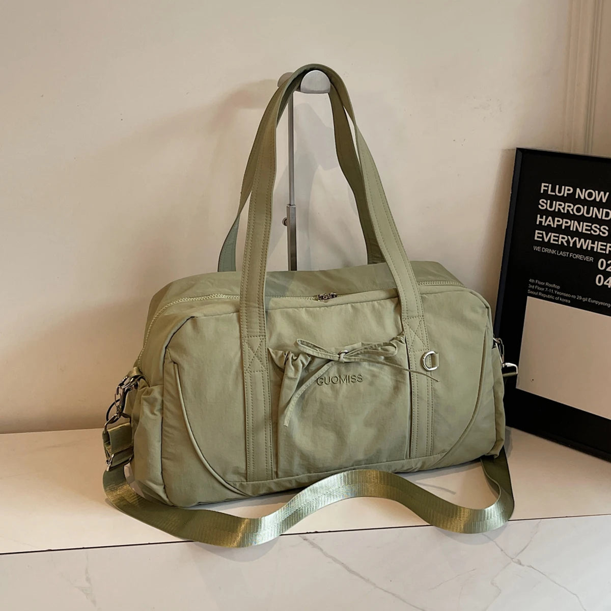 Olive green guomiss travel duffel bag made of nylon featuring a large capacity, drawstring front pocket, and adjustable shoulder strap designed for women.