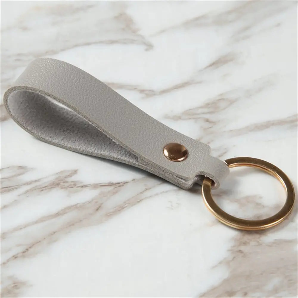 A sleek light gray pu leather keychain with a gold-toned metal ring and matching button fastening for secure hold.