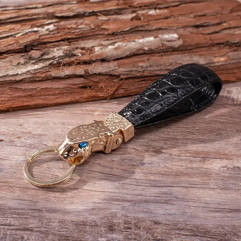 Black crocodile leather keychain with a gold-toned tiger head charm featuring blue gemstone eyes for luxury car key ring use.