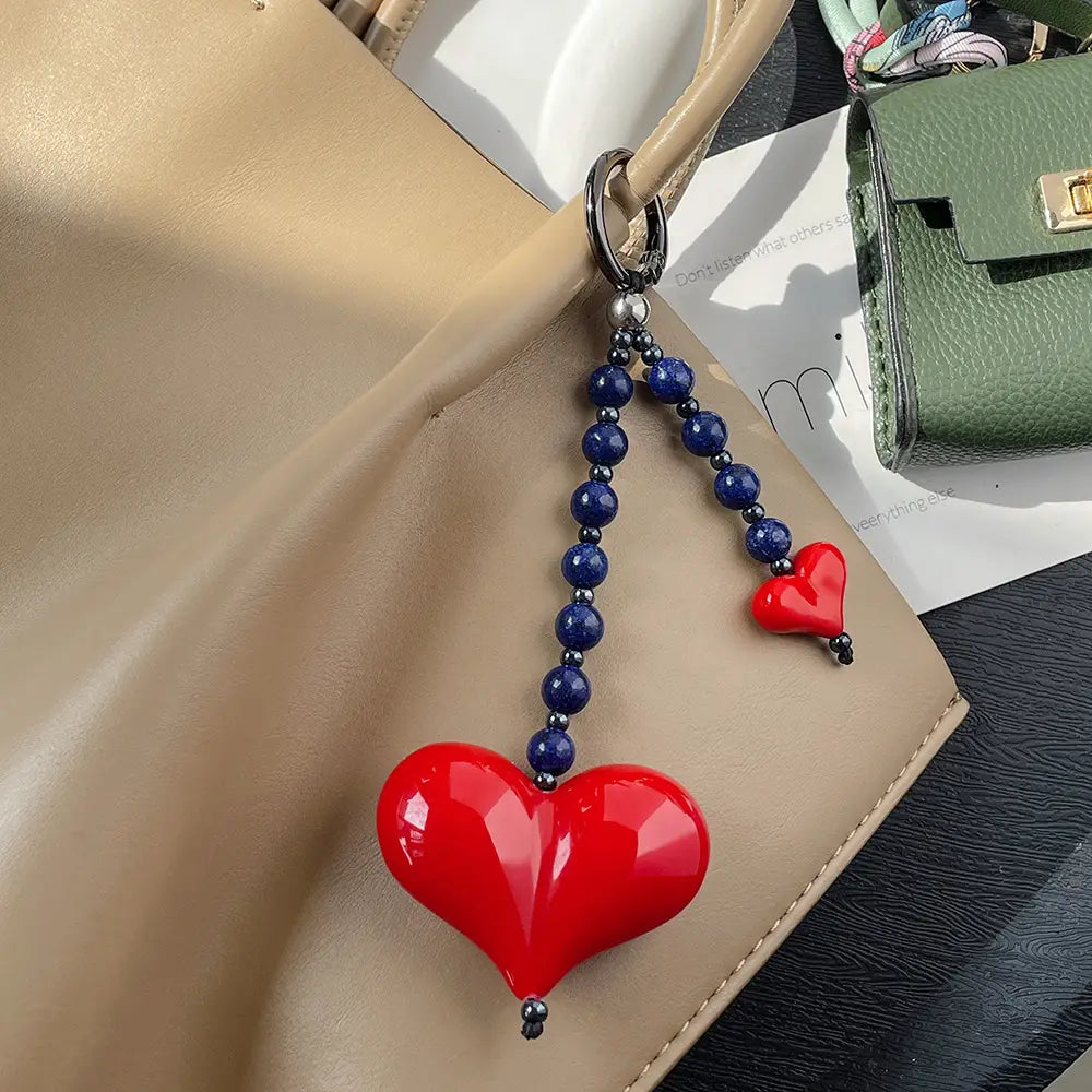 Porte-clés en forme de cœur rouge brillant, pendentif pour sac à perles, avec une chaînette pendante de perles bleu profond et de plus petites perles noires, fixées à un anneau en argent.