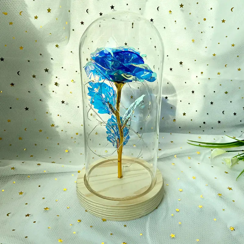 Eine kräftig blaue Glasrose mit goldenem Stiel, umschlossen in einer klaren Kuppel auf einem Holzsockel, im „Eternal Gold Rose Glass Dome Led Light Gift“.