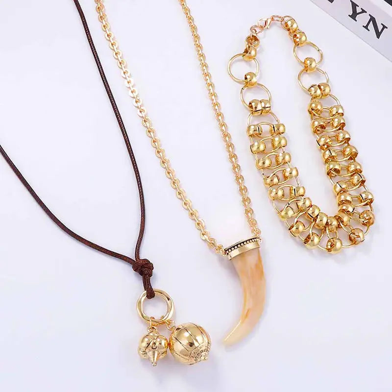 Vintage ethnic layered pendant necklace for women featuring a gold-toned chain with a curved light-colored horn pendant and two small golden charms hanging from a circular ring.