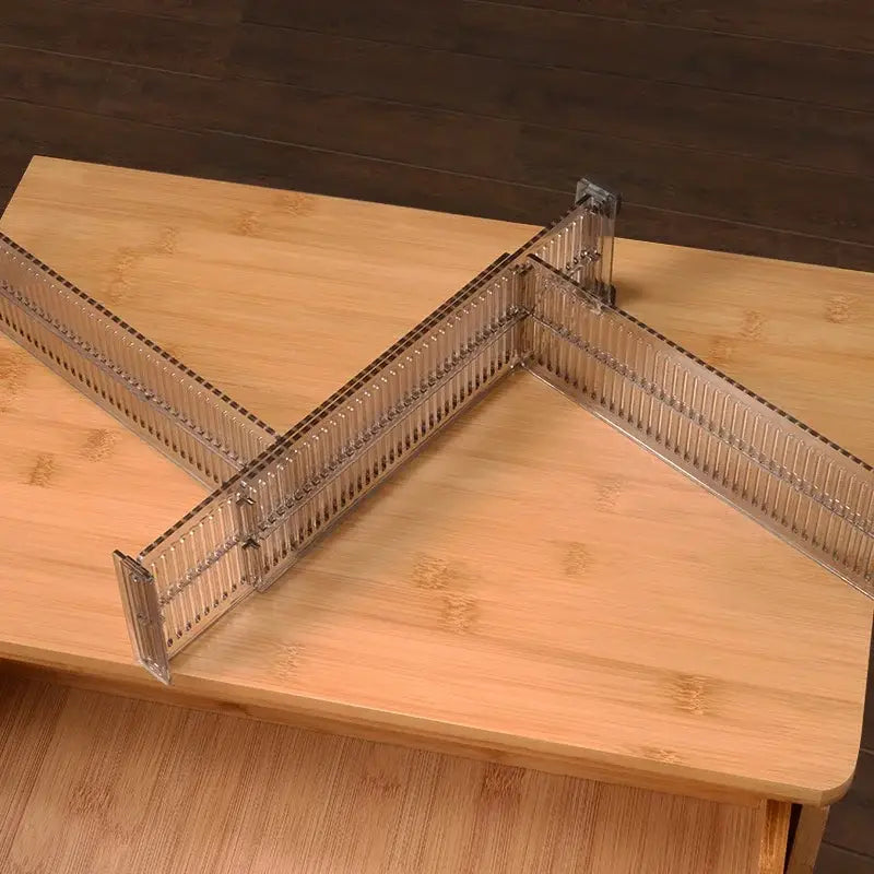 Clear plastic adjustable drawer partition storage divider with a grid x-shape design on a wooden surface.