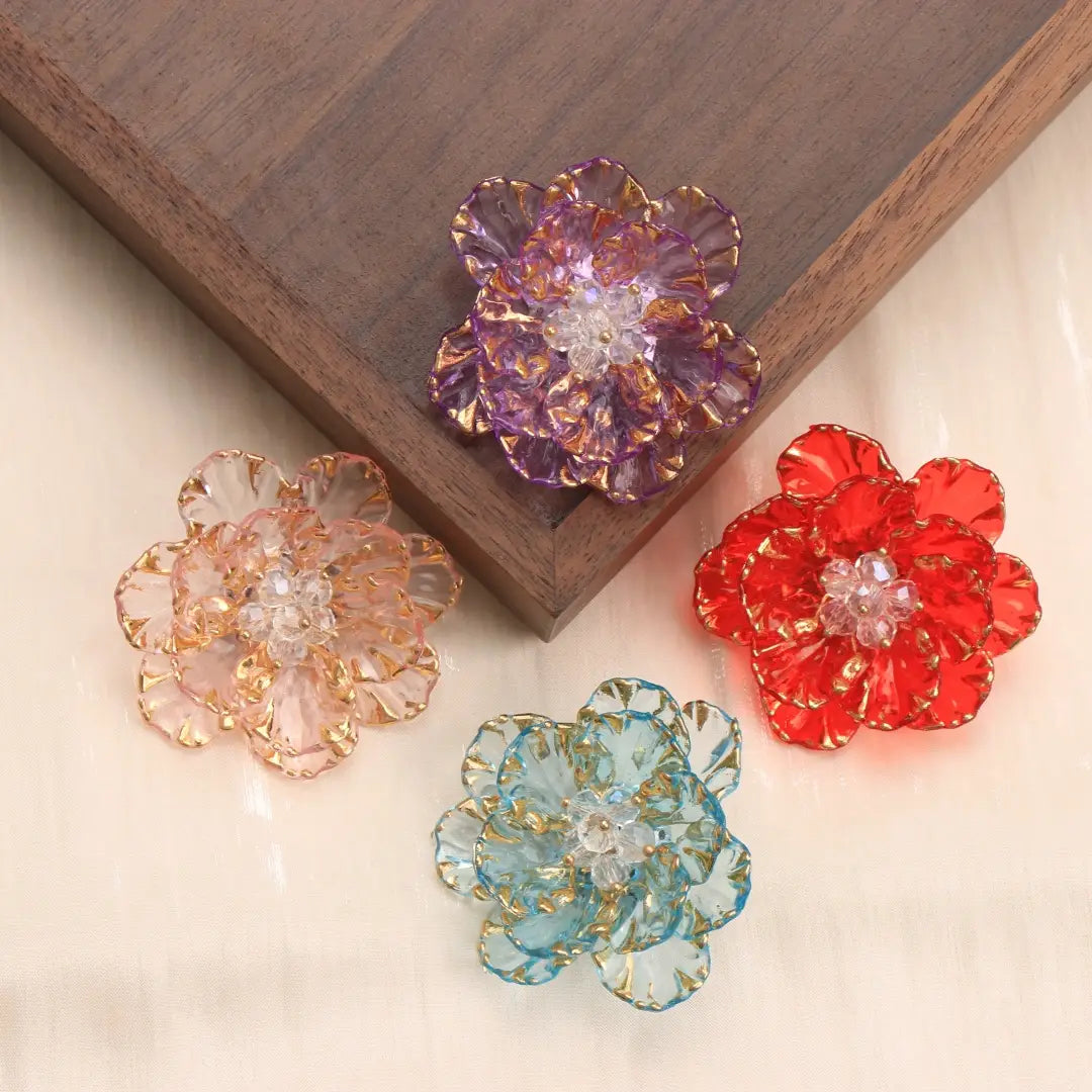 Trois épingles-broches en forme de fleur de cristal en verre translucide, en pourpre, pêche et rouge, avec des bords bordés d’or et des centres en cristal transparents, en tant qu’accessoires de mode.